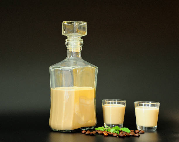 licor de café cremoso, garrafa, dois copos, um punhado de feijões torrados e folhas de hortelã em um fundo preto. - cream liqueur - fotografias e filmes do acervo