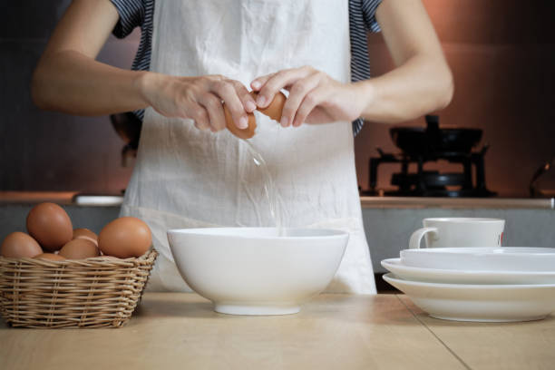 istock Female cook in a white apron is cracking an egg in home's kitchen. 1339184372
