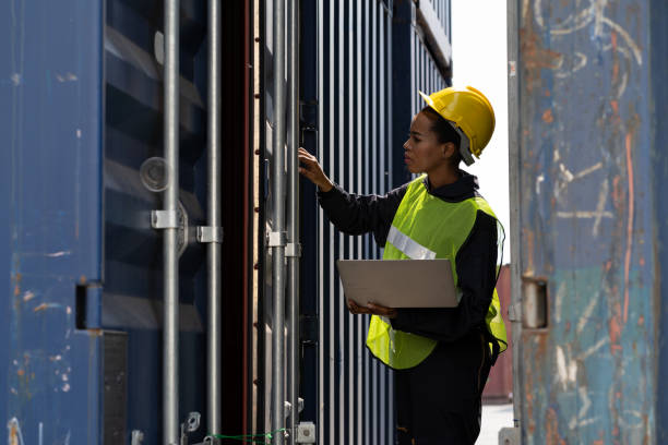 istock Female technician worker working at the commercial dock. African American female worker using computer laptop checking quality of steel container box from cargo freight at commercial dock site 1339187094