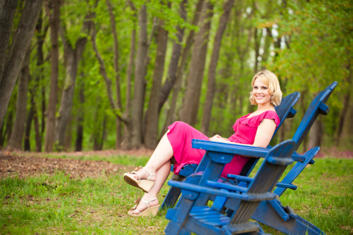 An early 30s attractive woman relaxing on an adirondock chair at a park in the spring.