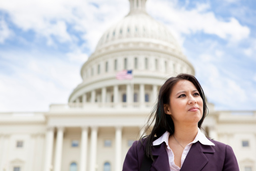 A Vietnamese businesswoman in her 30s looking away in front of the US Capitol building in Washington, DC.