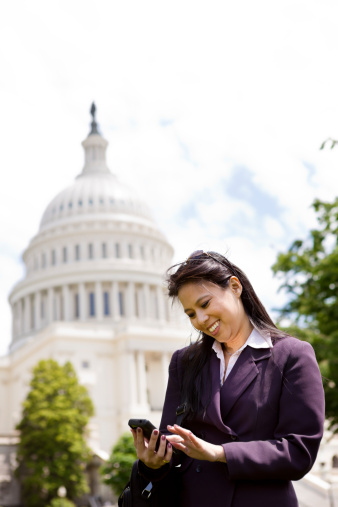 A Vietnamese woman wearing business attire touching phone in front of the Capitol building in Washington DC.