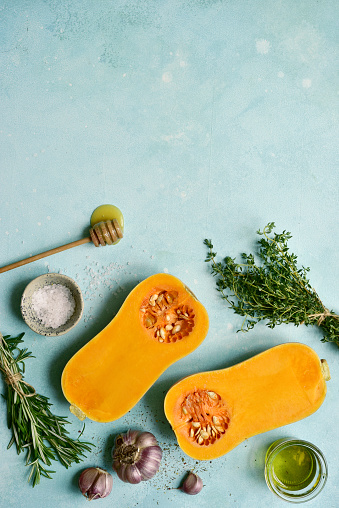 Halves of raw organic butternut squash with spices and ingredients for making on a blue slate, stone or concrete background. Top view with copy space.