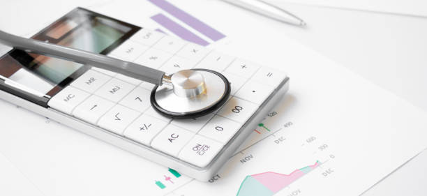 Financial health concept, stethoscope weaving around stacks of silver and gold coins and calculator stock photo