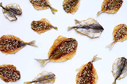 Dried fish with sesame seeds on white background.
