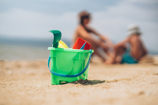 Beach toys in sand on the beach by the sea with mother and little child on the background.