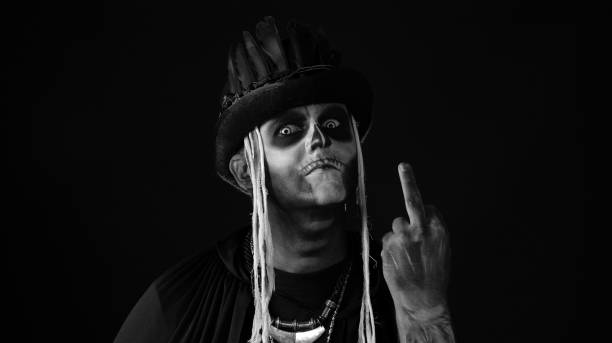 istock Sinister man with skull makeup making faces and showing middle finger. Bad manner gesture. Halloween 1339210953
