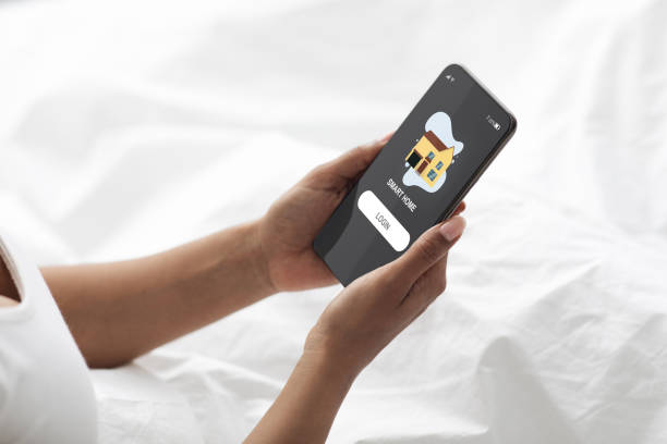 istock Black woman in bed login smart home system on cellphone 1339211297
