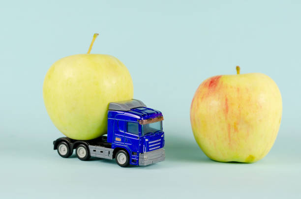 istock Toy truck pulling a ripe apple. Blue plastic truck and two fruit 1339211464
