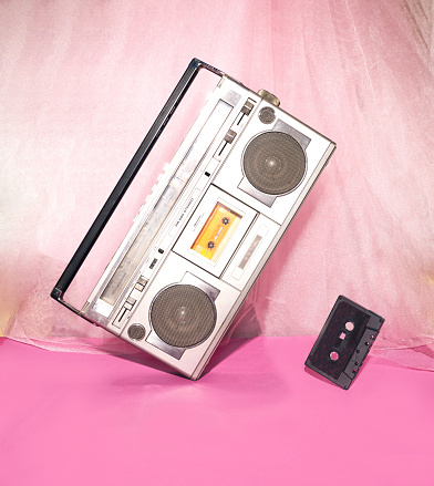 Funky music concept with silver cassette player and back cassete levitating against pink and purple background.