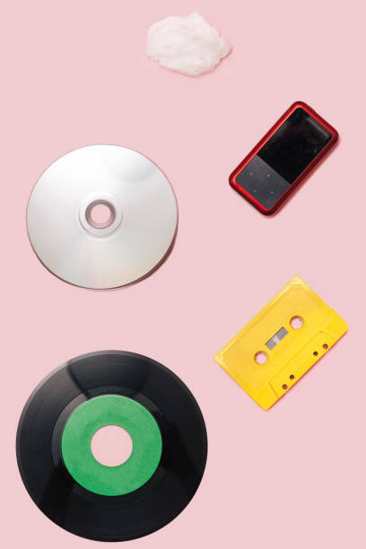 music mediums over time concept. ep and lp vinyl, cassette tape, cd, mp3 player, cell phone, portable speaker cotton cloud shaped prop flat lay arrangement against pink background. - cd player imagens e fotografias de stock