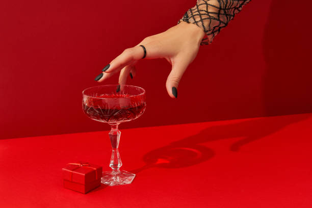 Womans hand with spooky nail design take glass with cranberry halloween cocktail on red background Womans hand with spooky nail design take glass with cranberry halloween cocktail on red background. Bloody party drink in a retro wineglass. red drink stock pictures, royalty-free photos & images
