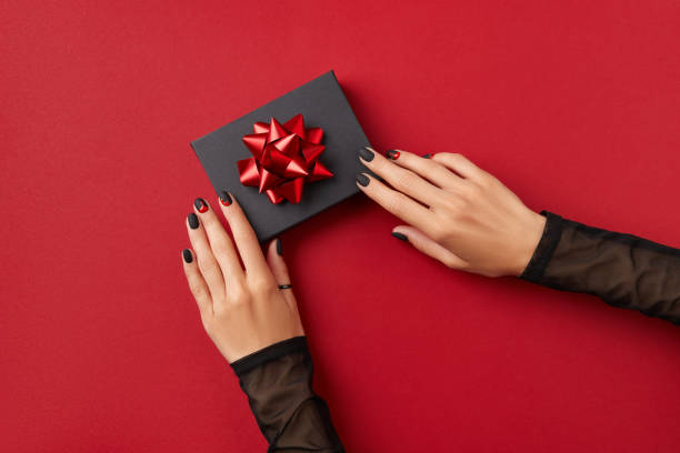 Beautiful groomed womans hands with gift box on red background. Halloween shopping sale concept Beautiful groomed womans hands with gift box on red background. Halloween shopping sale concept. Manicure, pedicure beauty salon template fall nail art stock pictures, royalty-free photos & images