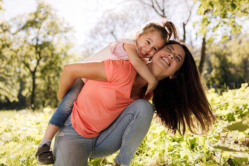 Happy little girl embracing her mother with great affection during spring day at the park.