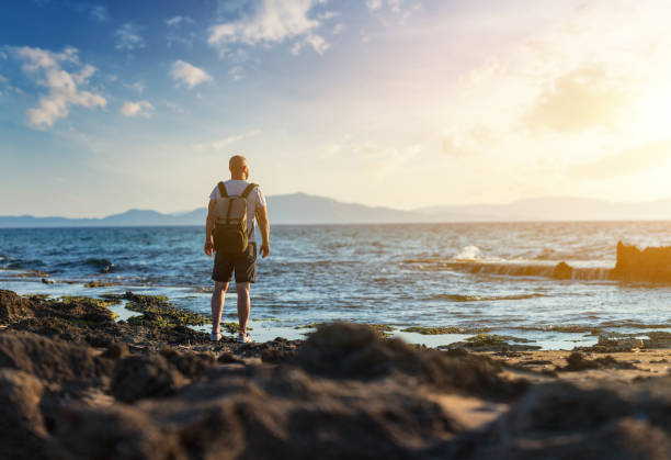 istock Man stands alone at the rocky beach at sunset 1339224404