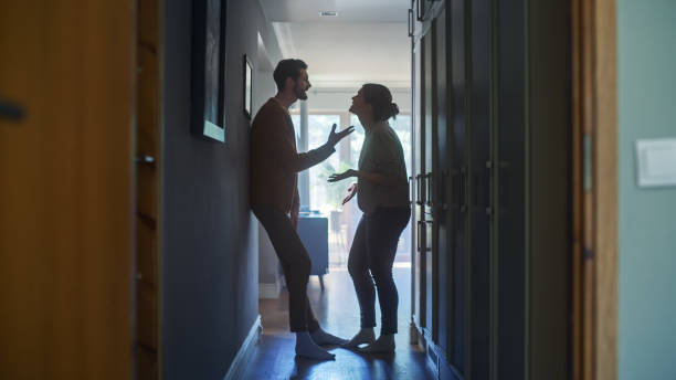 young couple arguing and fighting. domestic violence scene of emotional abuse, stressed woman and aggressive man having almost violent argument in a dark claustrophobic hallway of apartment. - ruzie stockfoto's en -beelden