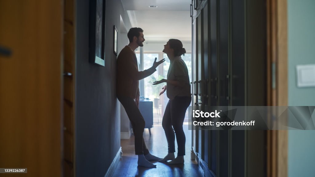 Young Couple Arguing and Fighting. Domestic Violence Scene of Emotional abuse, Stressed Woman and aggressive Man Having Almost Violent Argument in a Dark Claustrophobic Hallway of Apartment. Couple - Relationship Stock Photo