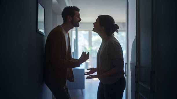 jeune couple se disputant et se disputant. scène de violence domestique et de violence émotionnelle, femme stressée et homme agressif se criant dessus dans le couloir sombre de l’appartement. scène dramatique - arguing photos et images de collection