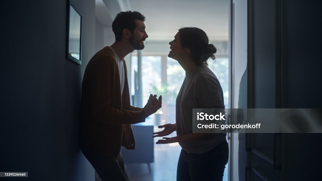 Young Couple Arguing and Fighting. Domestic Violence and Emotional abuse Scene, Stressed Woman and aggressive Man Screaming at Each other in the Dark Hallway of Apartment. Dramatic Scene Couple - Relationship Stock Photo