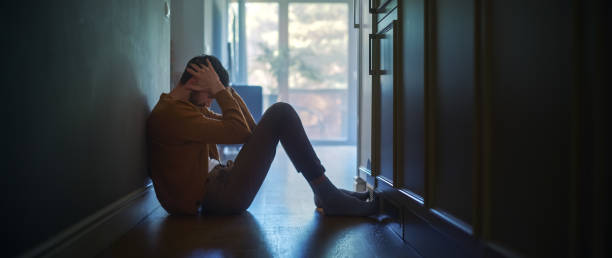 悲しい中年男性は、彼のアパートの廊下で床に座って、 手で顔を覆います。うつ病、病気、悲劇、家族の死の雰囲気。ドラマチックな悪いニュースモーメント - anxiety ストックフォトと画像