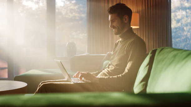 istock Man Using Laptop at Home, Does Remote Work. Handsome Male Sitting on Sofa Works On Computer, Brainstorms Creative Project, Online Data and Information Research. Productive Work in Sunny Living Room 1339226584