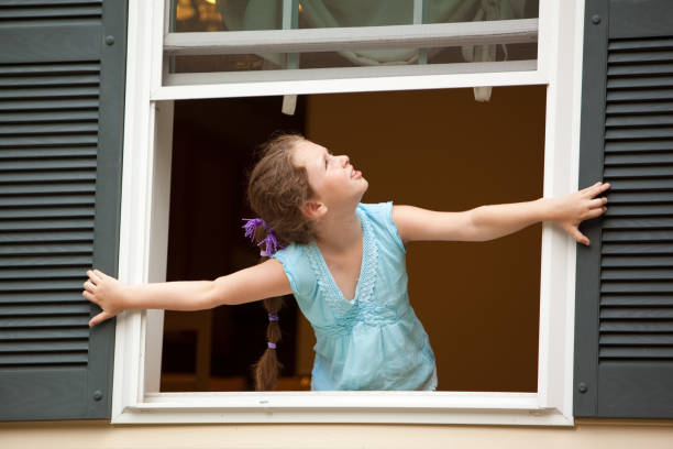 Little girl looking from the open window of country house