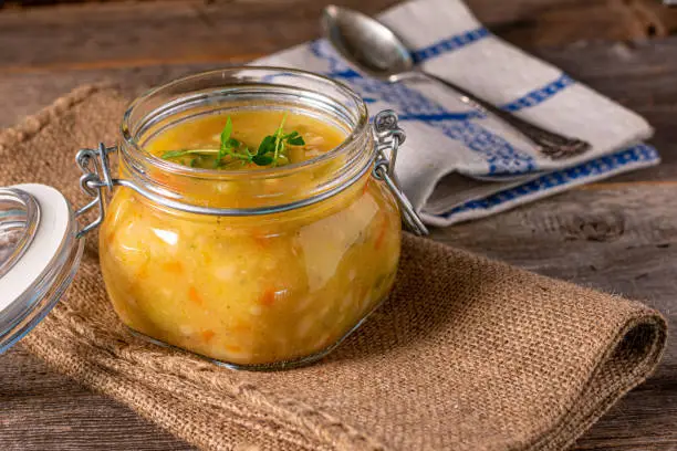 Fresh and homemade cooked soup or stew in a  jar served isolated on rustic and wooden table. Closeup view