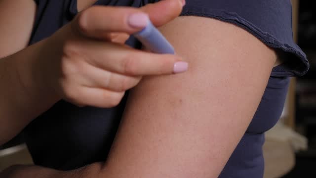 Close-up of a young woman injecting insulin into her arm with an insulin pen.