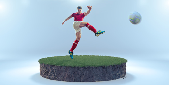 A studio image of a male football player wearing generic red and white kit, with right leg up having just kicked a soccer ball in a volley above a circular cross section of ground consisting of grass on top of a depth of mud. With motion blur to ball.