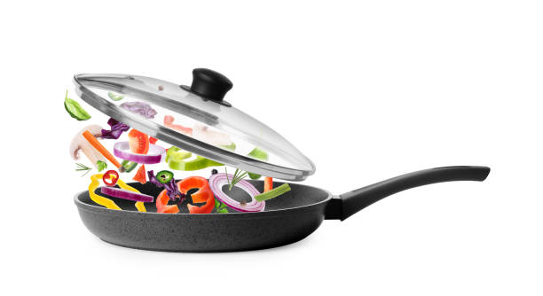 istock Different vegetables falling into frying pan on white background. Process of cooking 1339241542