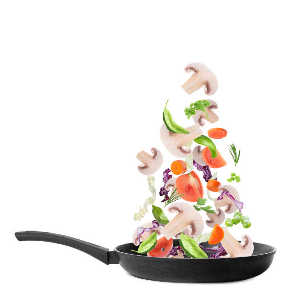 istock Different vegetables and mushrooms falling into frying pan on white background. Process of cooking 1339241595