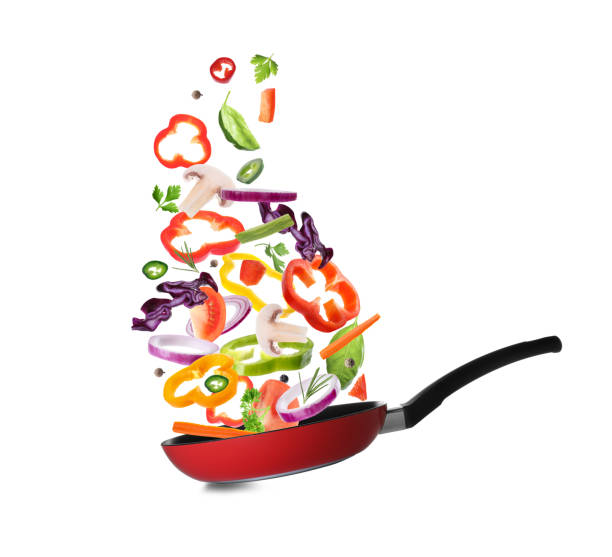 istock Different vegetables falling into frying pan on white background. Process of cooking 1339241707