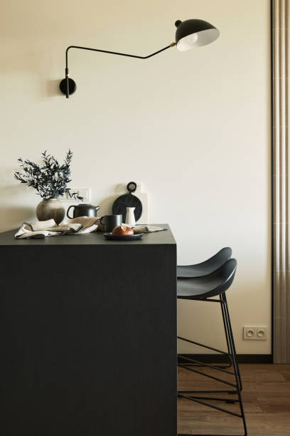 istock Stylish composition of modern kitchen and dining room interior in small apartment. Black furniture, kitchen island and wooden kitchen accessories. Creative wall. Template. 1339241857