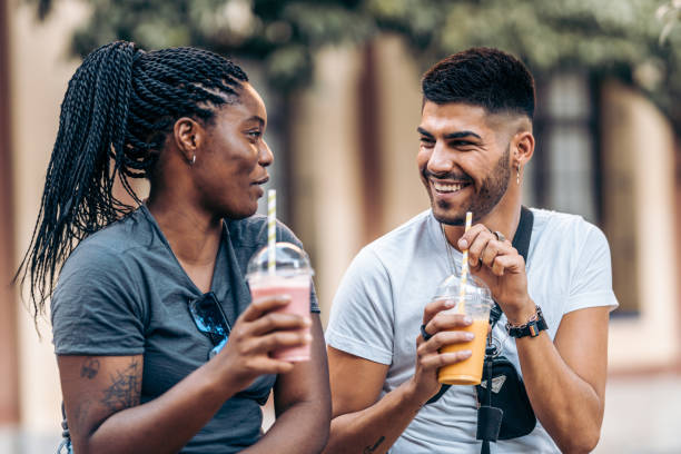 Young caucasian man and young black woman drinking a milkshake in the street Young caucasian man and young black woman drinking a milkshake in the street while chatting happily body adornment rear view young men men stock pictures, royalty-free photos & images