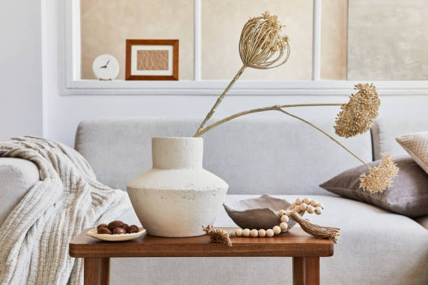 istock Creative composition of stylish and cozy living room interior with mock up frame, grey sofa, window, dried flowers in vase and personal accessories. Beige neutral colors. Details. Template. 1339247070