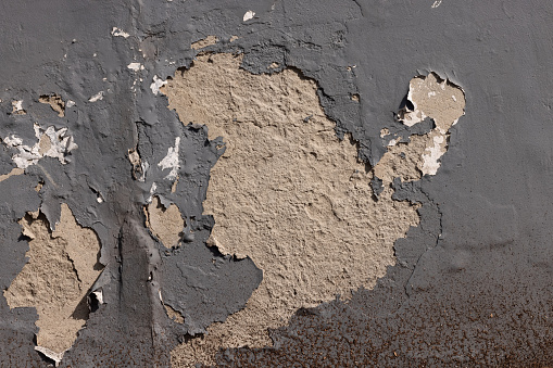 Part of an old gray concrete wall with cracked and peeling paint.