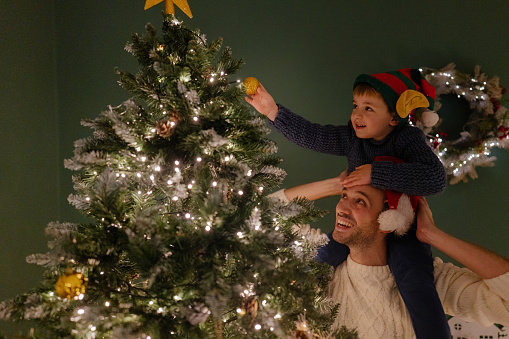 Photo of a cute little boy, decorating Christmas tree with a help from his father