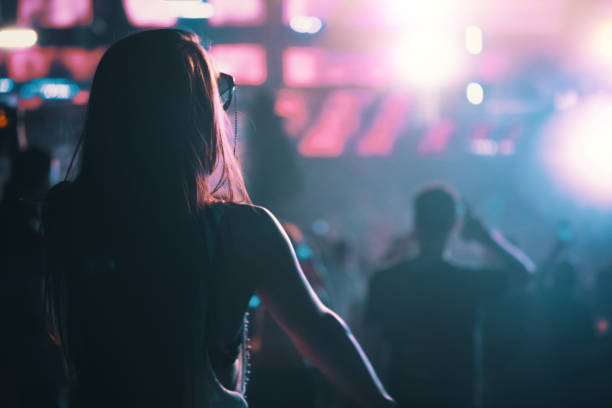 Woman enjoying a concert party Closeup rear view of a late 20's woman dancing at a rave party. festival goer stock pictures, royalty-free photos & images