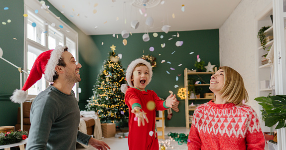 Photo of a young family, being festive on Christmas morning. Boy is throwing confetti while still in pyjamas.
