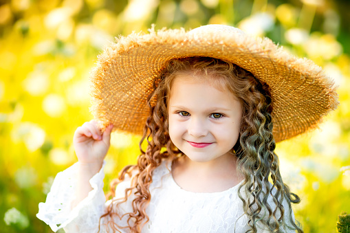 cheerful beautiful girl in a straw hat in summer in a yellow field with flowers