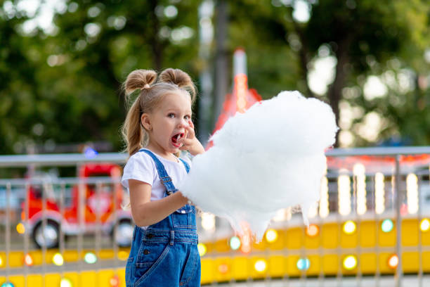 happy baby girl eating cotton candy at amusement Park in summer happy baby girl eating cotton candy at amusement Park in summer child cotton candy stock pictures, royalty-free photos & images