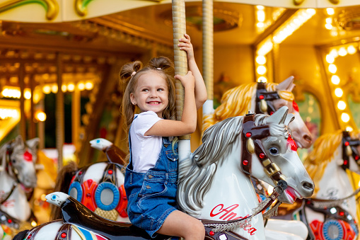 Chica feliz en un parque de atracciones monta a caballo en un carrusel en el verano photo
