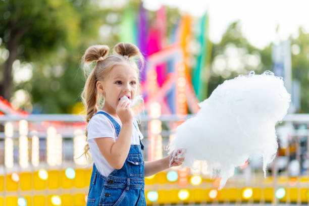 happy baby girl eating cotton candy at amusement Park in summer happy baby girl eating cotton candy at amusement Park in summer child cotton candy stock pictures, royalty-free photos & images
