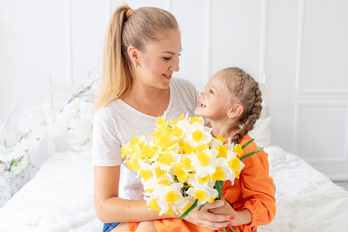 baby girl gives flowers to her mother for a holiday on the bed at home, the concept of love and motherhood or mother's day