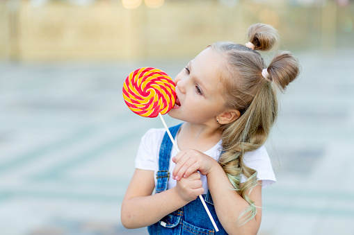 portrait of a child girl with a large Lollipop in the summer on the street