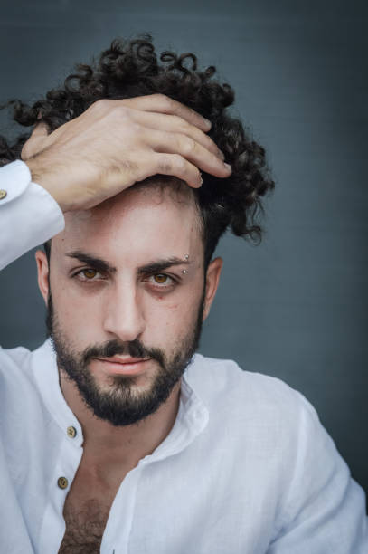 ritratto di un giovane con la barba, che con la mano tiene i capelli ricci che gli coprono la fronte - fashion male beauty confidence elegance foto e immagini stock