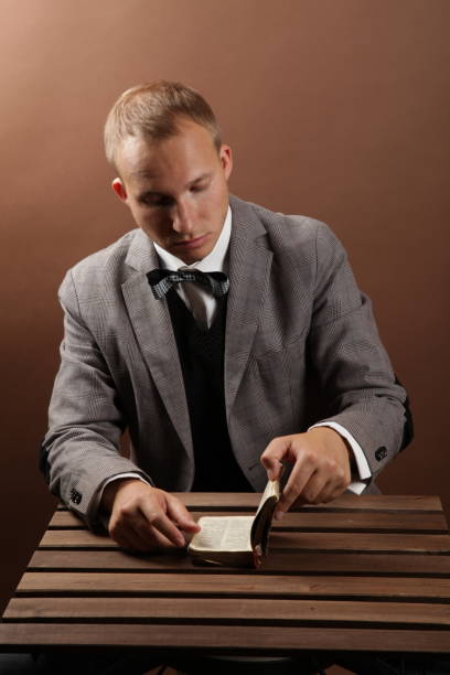 istock A handsome, confident businessman in a suit, sitting alone on a brown background and reading a book. Next to a wooden table 1339263103