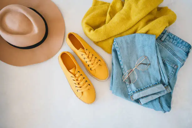 Flat lay with woman's clothes and accessories: jeans, sneakers, sweater and fedora hat
