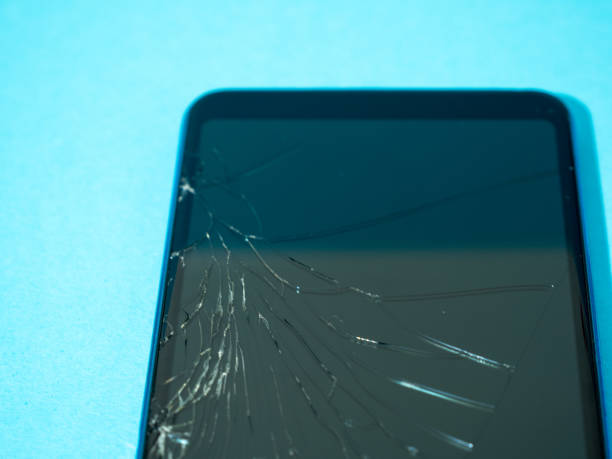 istock Black crashed smartphone with broken screen and body on a blue table in service. 1339266649
