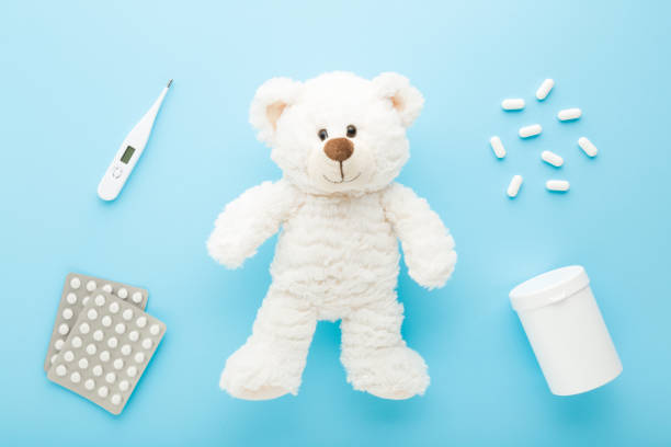 istock White teddy bear, digital thermometer, plastic bottle and blister packs with pills on light blue table background. Pastel color. Closeup. Child treatment concept. Top down view. 1339267027